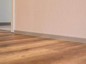 Flache Sockelleiste aus Aluminium als Wandabschluss auf verlegtem Designboden in Eichenoptik