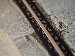 Dehnungsfugenprofil aus schwarzem Kunststoff und silberner Sichtleiste auf einem vorbereiteten Estrichboden