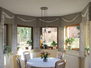 Helles Esszimmer mit großen Fenstern, Pflanzen und Blumenvase auf Tisch.