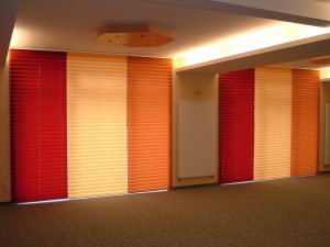 Moderne Raumgestaltung mit farbigen Faltstores in Rot, Orange und Beige.