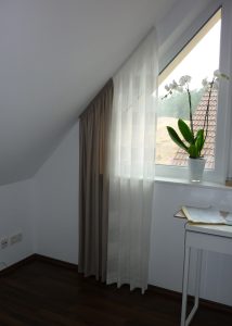 Helles Zimmer mit Fenster, Vorhängen und Orchidee auf Tisch.