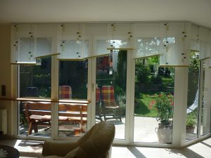 Wohnzimmer mit Flächenvorhänge vor Panoramafenstern und Blick auf den Garten