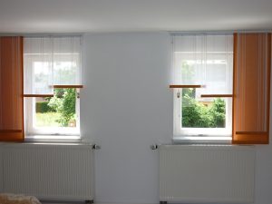 Fenster mit weißen und orangen Vorhängen und Blick auf grüne Natur im Wohnzimmer.