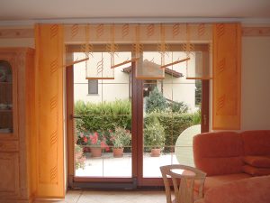 Fenster mit gelben Flächenvorhängen, Blick auf Terasse mit Pflanzen