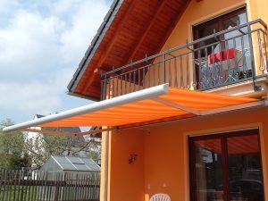 Haus mit Balkon und orangefarbener Markise, sonniger Außenbereich, modernes Design.