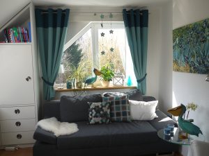 Helles Zimmer mit Sofa, Dekorationen und Fenster mit Ösenschal.